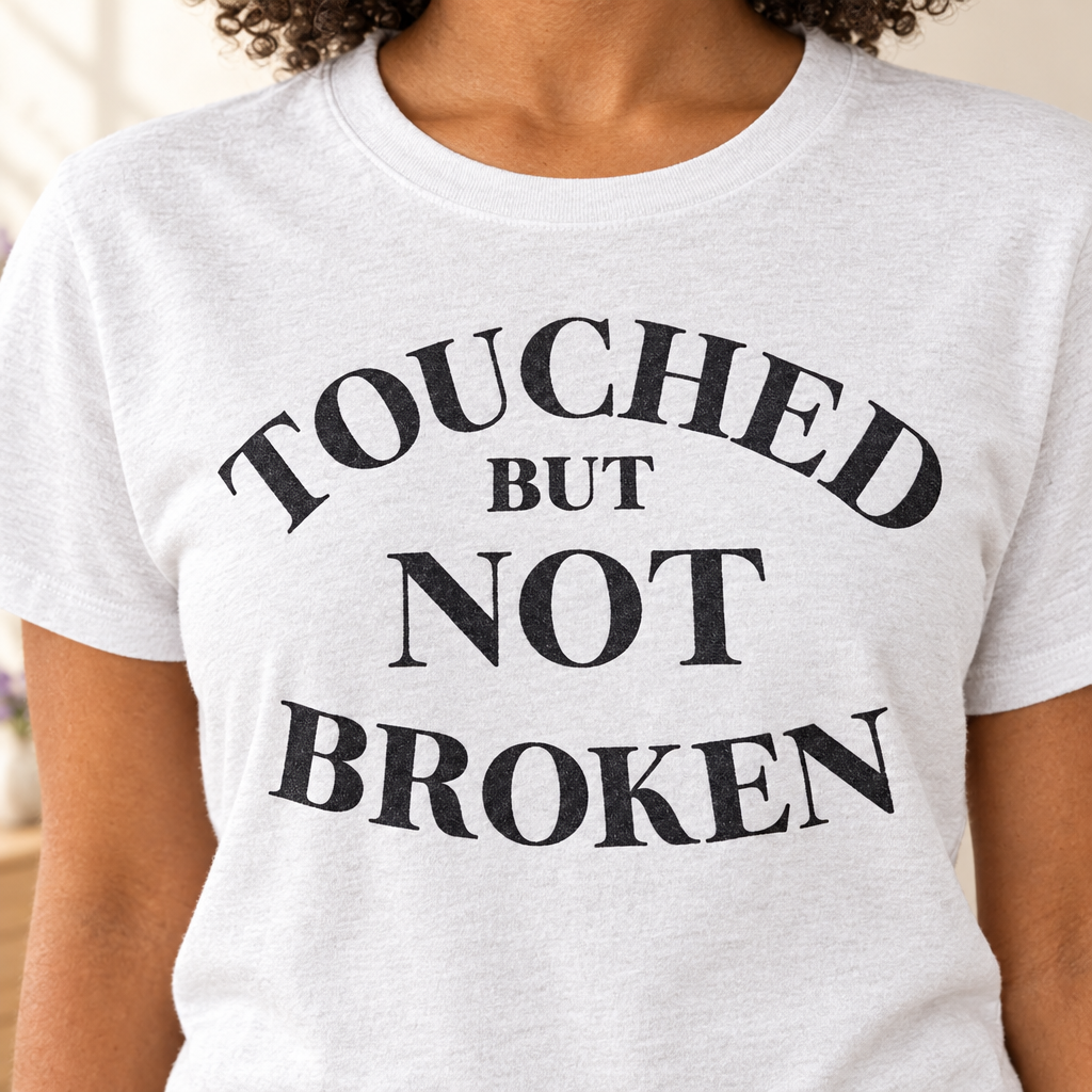Touched But Not Broken Tee in light gray cotton with bold black serif lettering arranged in arched lines across the chest.